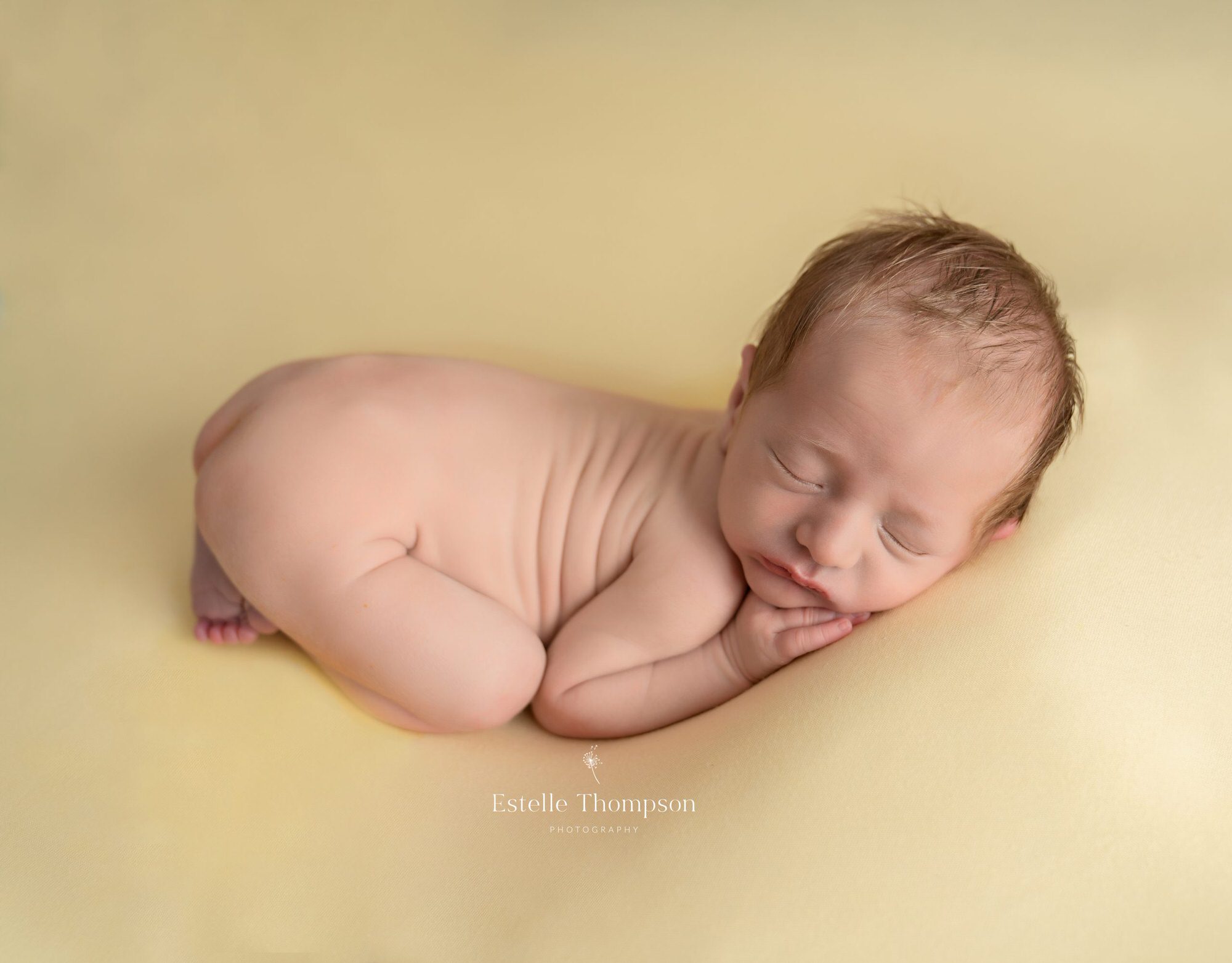 A newborn baby boy sleeps curled up on a yellow blanket by Sevenoaks newborn photographer