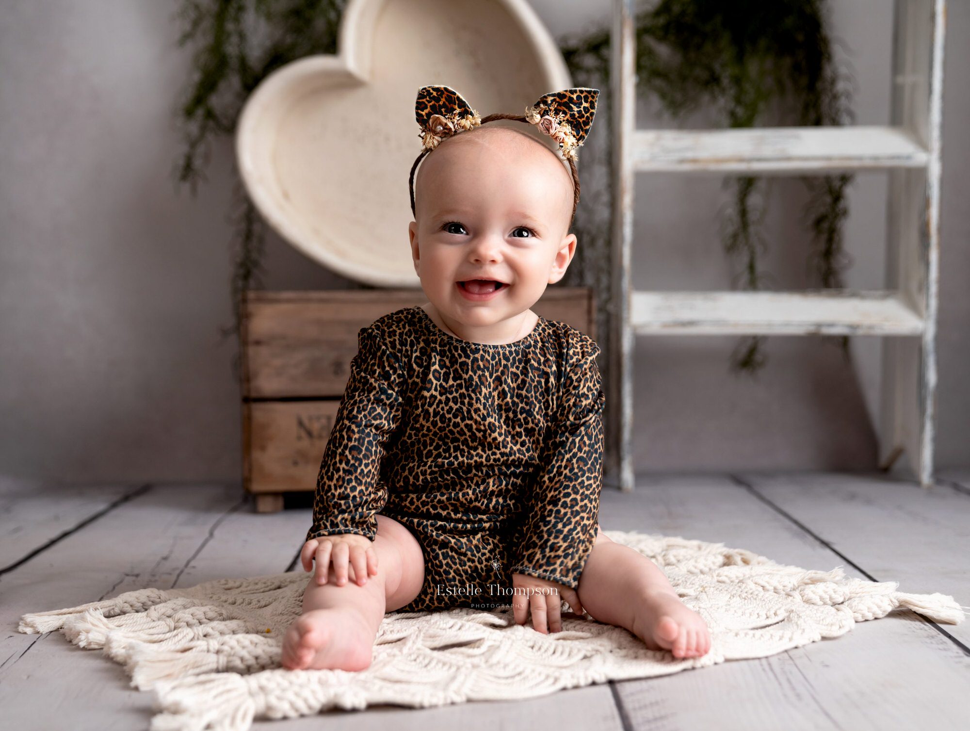 Baby girl wearing a leopard print romper sits on the floor laughing by Sevenoaks baby photographer