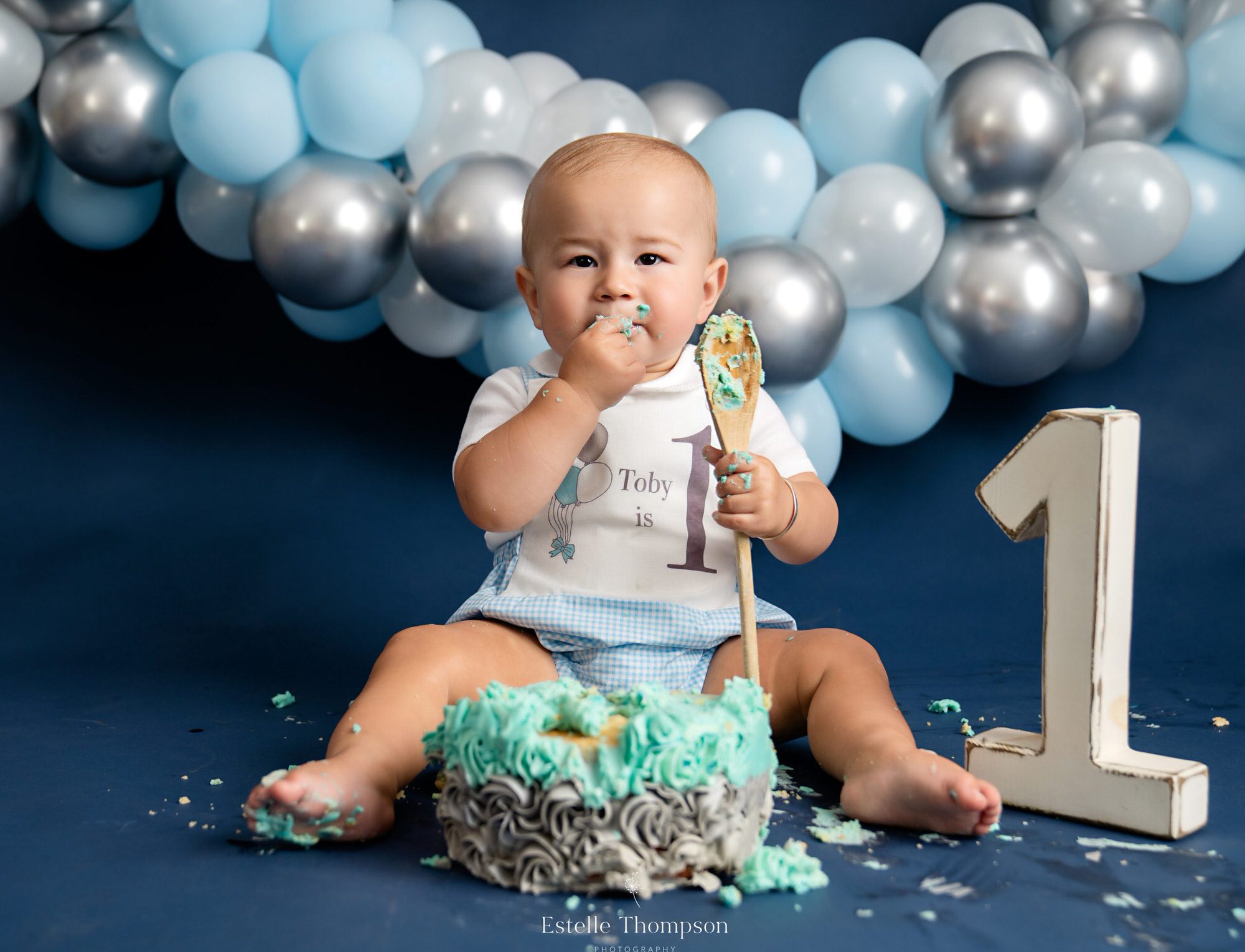 A baby boy sits in front of a cake he is eating at a sevenoaks cake smash photoshoot