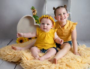Two sisters dressed in yellow sit to have their photograph taken at a sevenoaks baby photography studio