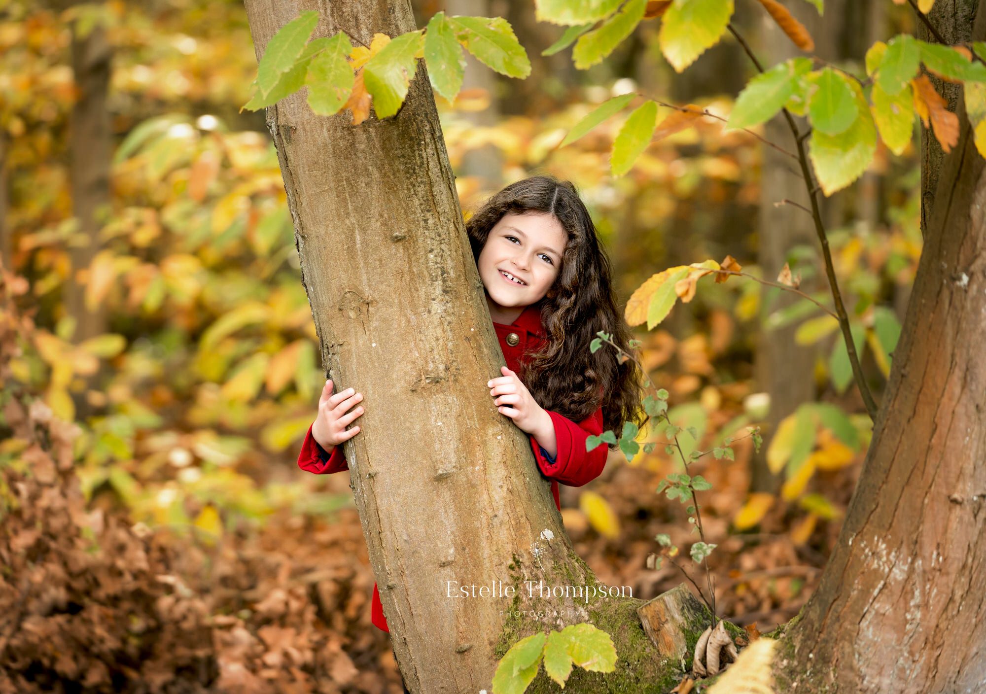 A little girl plays hide and seek behind a tree with her Sevenoaks family photographer