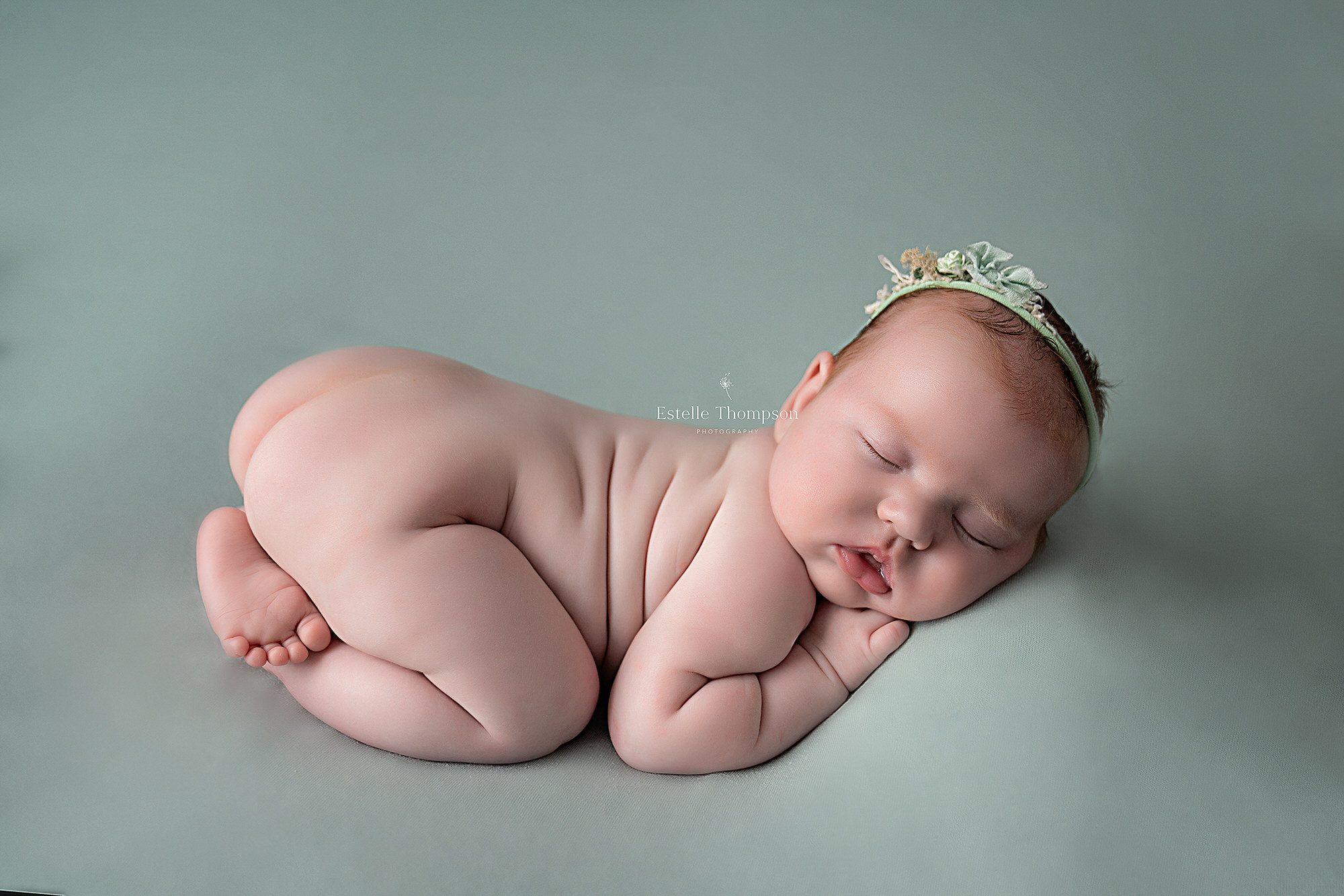 a newborn baby girl lays on a mint green blanket with her legs crossed under her bottom while a longfield newborn photographer takes her photoshoot