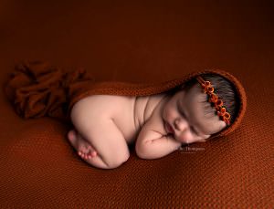 Baby girl laying on an orange backdrop in Sevenoaks newborn photographer studio