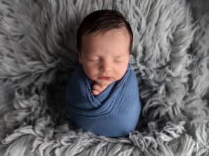 Baby boy wrapped in a blue cloth sleeping on a blue blanket in a Sevenoaks Newborn Photographer Studio