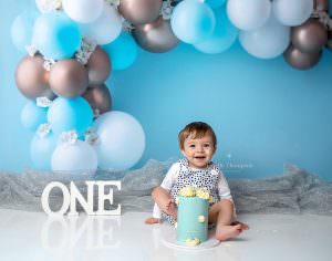 Baby boy against a blue backdrop with his first birthday cake