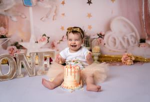 Baby girl with wearing a peach tutu on her first birthday cake smash shoot
